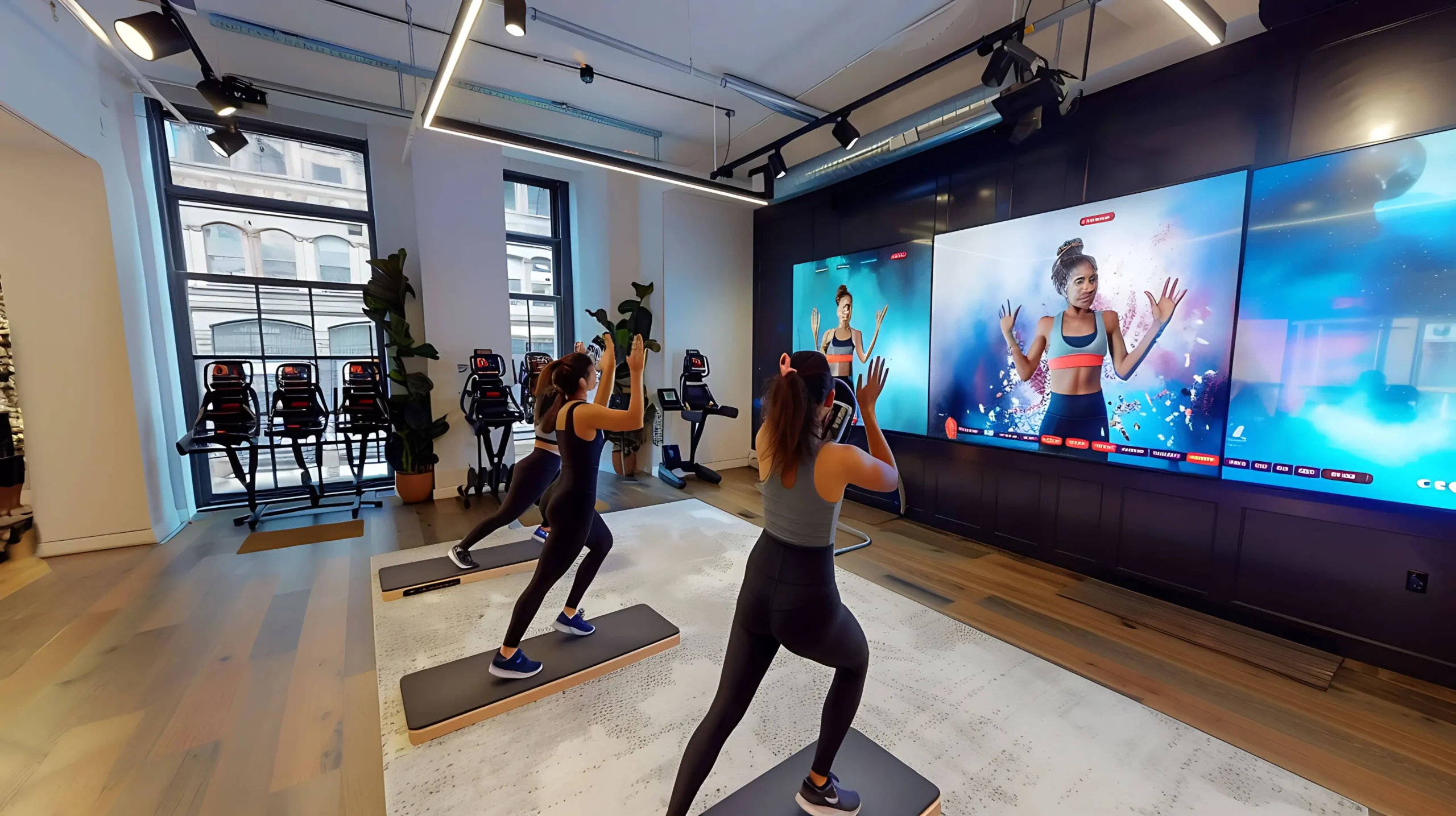 People exercising in a gym in front of a large indoor LED video wall showing a fitness class
