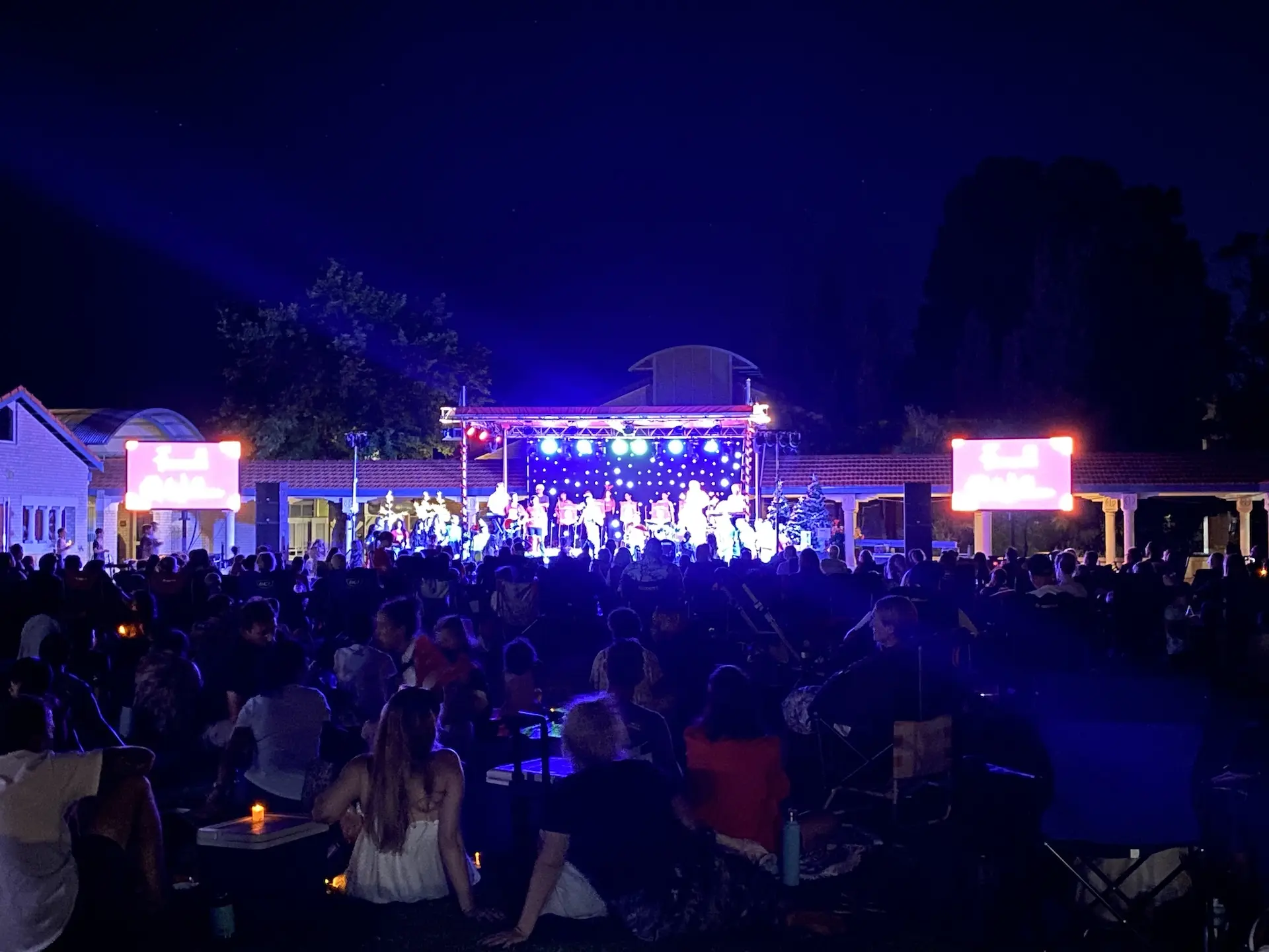 Nighttime outdoor school concert with a crowd and two LED screens beside the stage