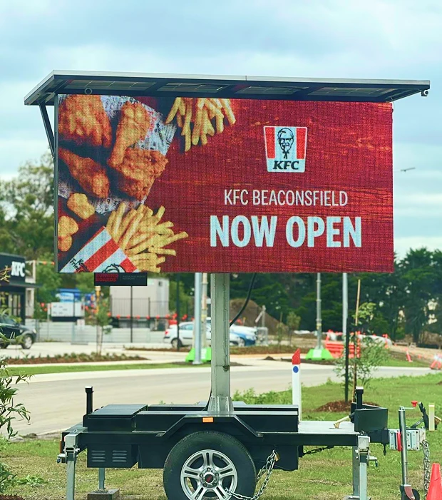 Trailer-mounted LED billboard displaying a KFC now open advertisement beside a road