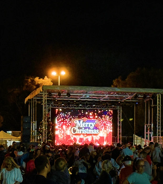 Crowd at a nighttime event watching a stage LED screen displaying a Merry Christmas message