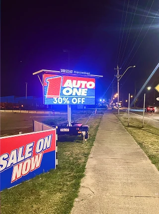Roadside trailer-mounted LED billboard at night displaying an Auto One sale advertisement